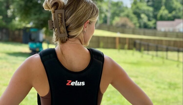 Woman seen from behind wearing a black Zelus weighted vest on a grassy field